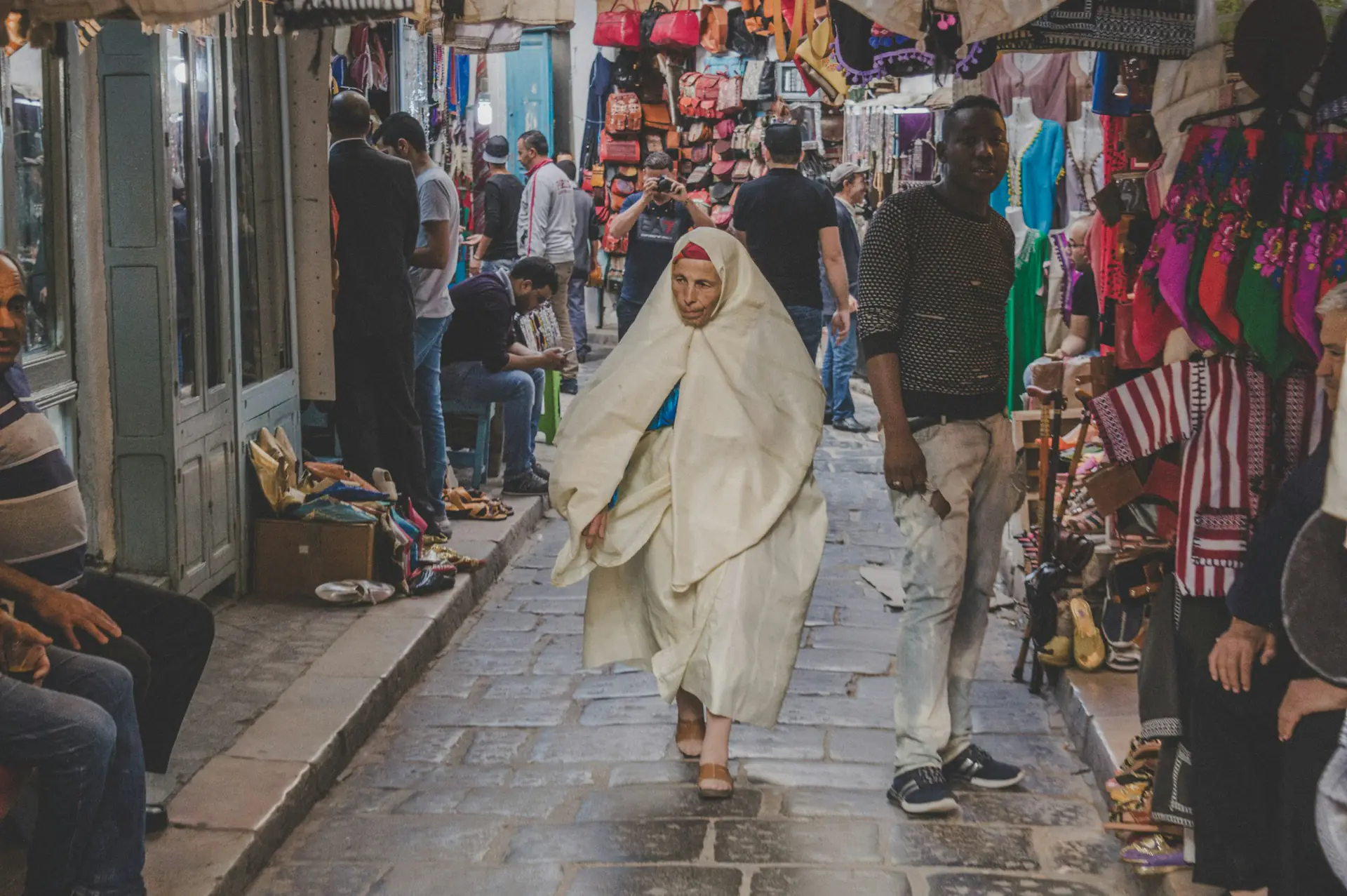 Shoppers and a woman in a white safsari in a souk of the Medina of Tunis
