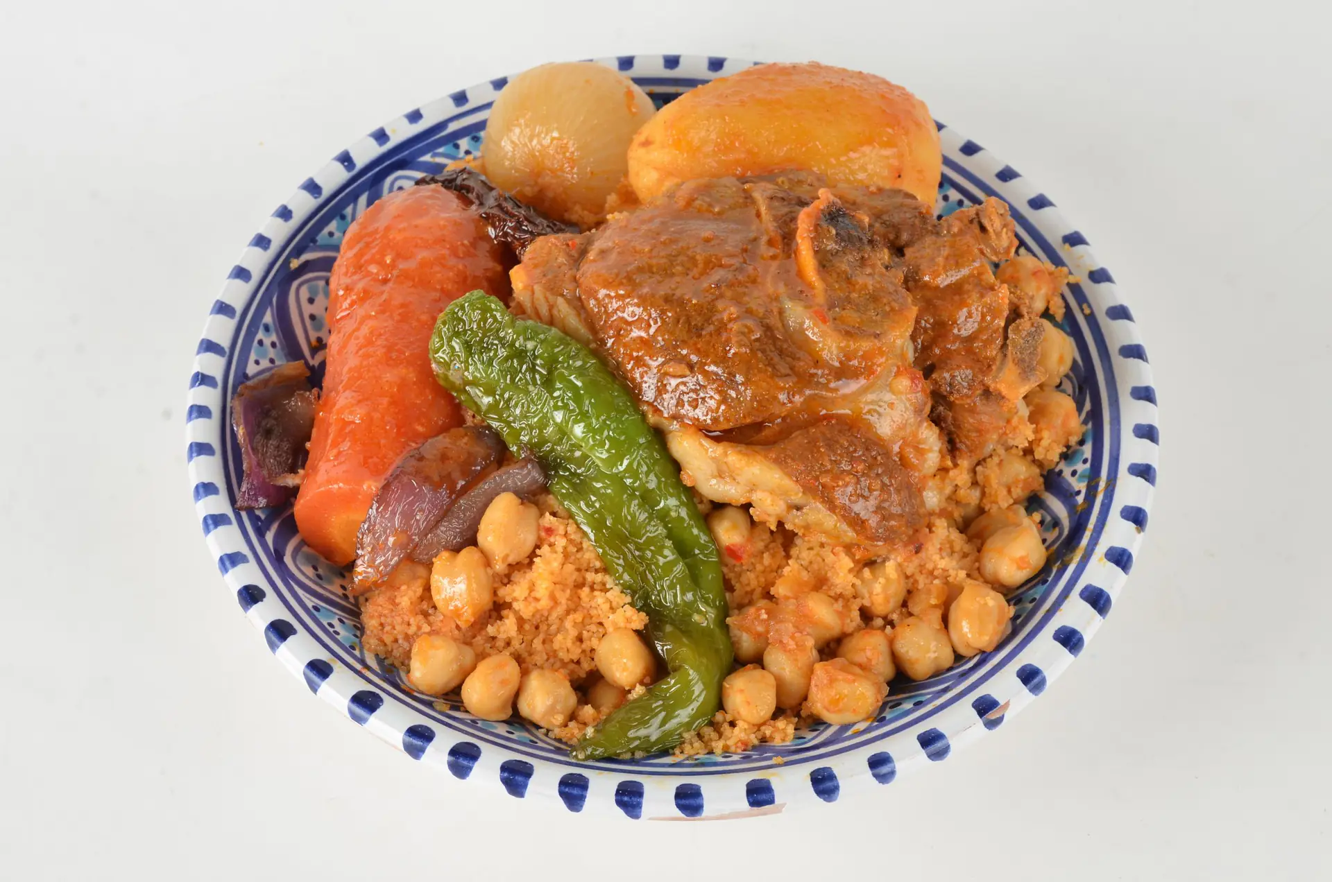 Couscous with meat, vegetables, chickpeas and a green pepper on a painted plate