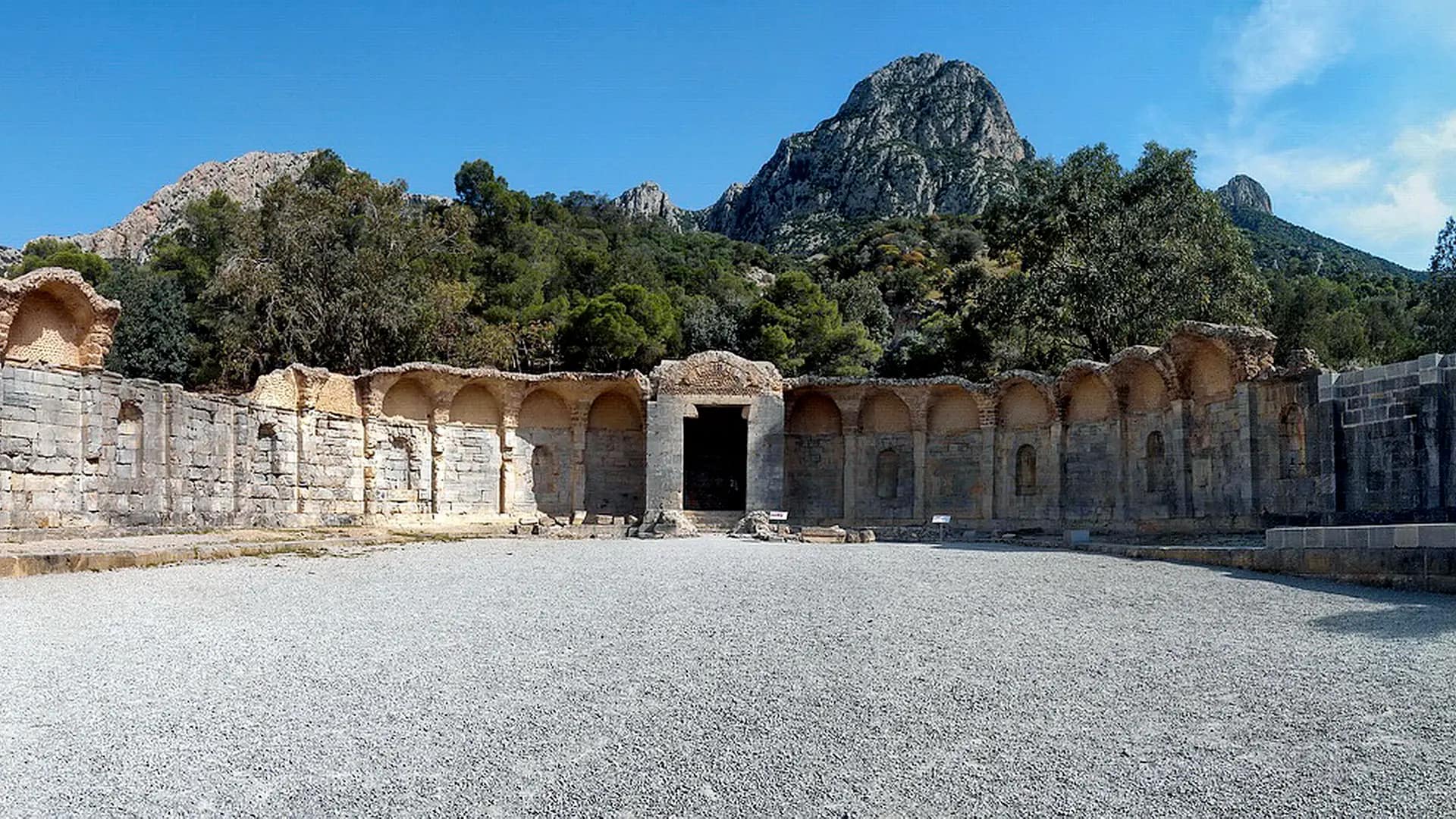 The semicircle of arcades around the Roman Temple of Waters in Zaghouan, below wooded hills